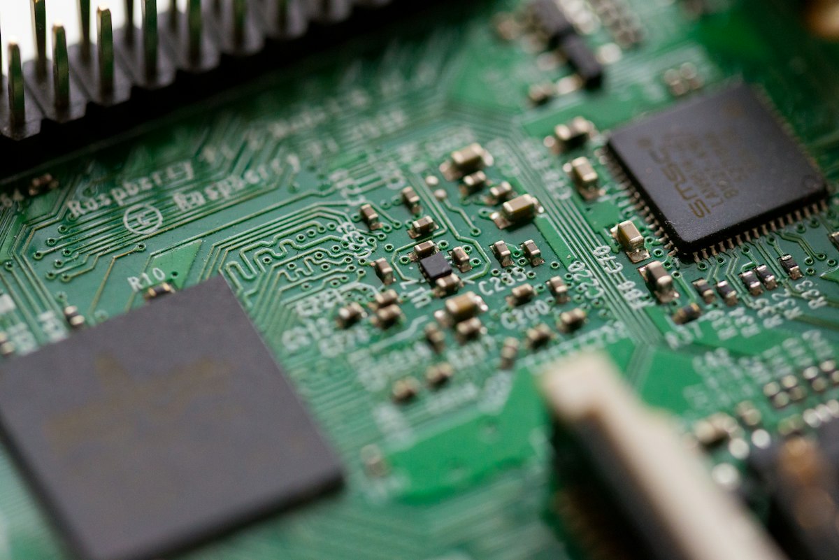 Macro close-up of a green printed-circuit board with chips and capacitors — generic electronics stock photo illustrating the open-hardware section below, not a photo of the FeSens openTPU board, its FPGA card, or any real hardware