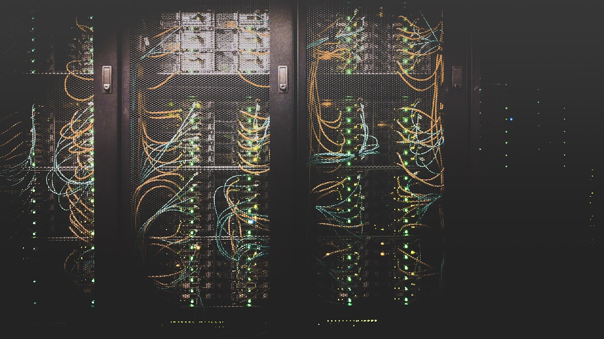 Stock photo of data-center server racks with cabling and blinking LEDs, evoking the scale of large-model GPU hosting — not a table of actual hardware requirements